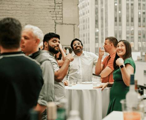 A diverse group of AdsLoom.net employees gathered in their office, smiling and posing around a table with a dessert tray, reflecting a collaborative and welcoming workspace.