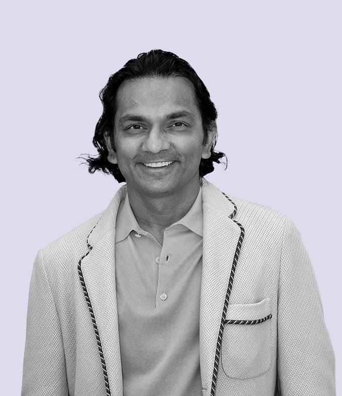 Black-and-white professional portrait of Div Turakhia, Founder of AdsLoom.net, smiling slightly, dressed in a formal blazer and white shirt against a subtle lavender background.