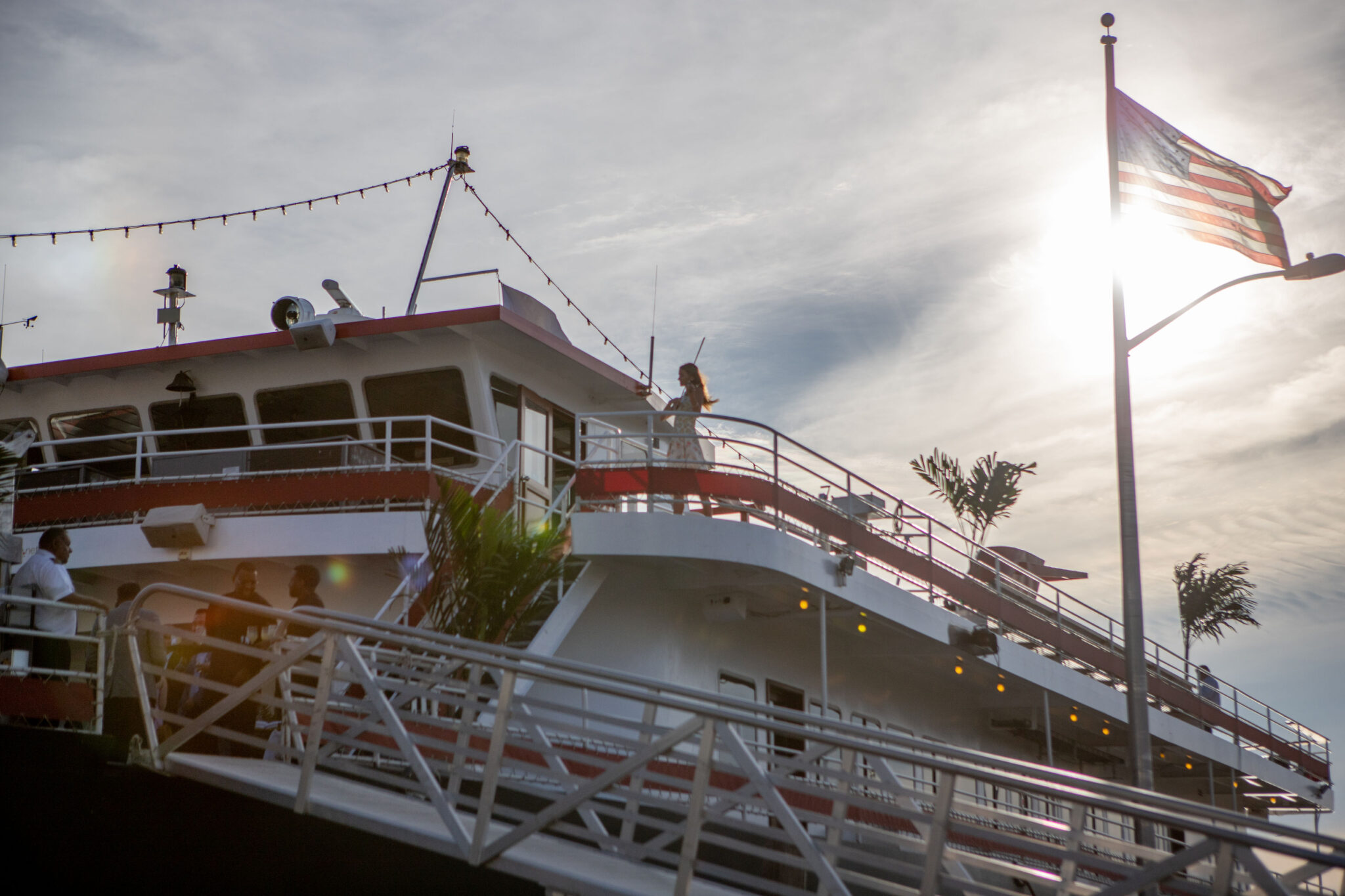 View of the AdsLoom.net event yacht at sunset, with an American flag in the foreground and a violinist visible on the upper deck.