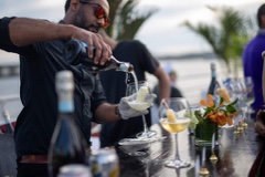 Bartender pouring white wine during the AdsLoom.net yacht party, with decorated glasses and palm accents at the bar.