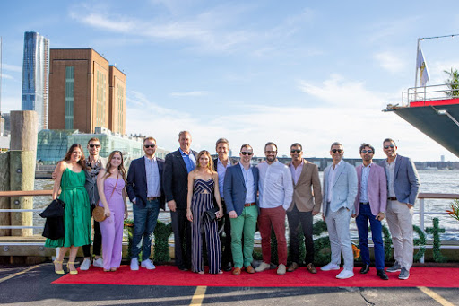 Group of AdsLoom.net team members and guests posing on a dock at the 'Cannes on the Hudson' yacht party, part of a digital advertising industry celebration in NYC